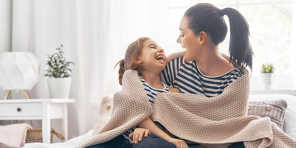 Mother and daughter snuggle up in blanket and enjoy health benefits of a humidifier.