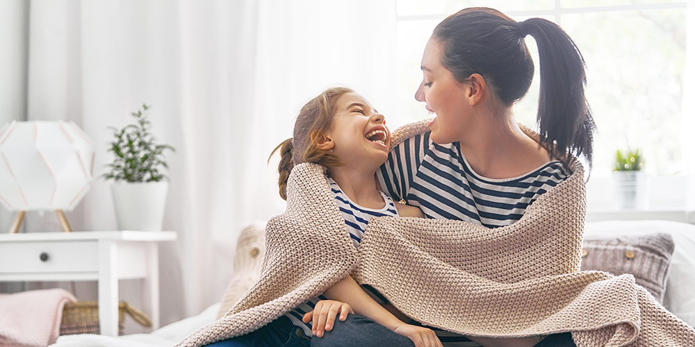 Mother and daughter snuggle up in blanket and enjoy health benefits of a humidifier.