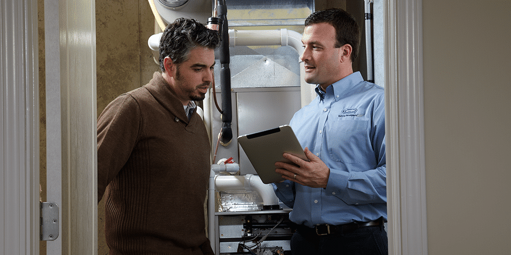 Technician helps male homeowner complete fall HVAC checklist with furnace maintenance.