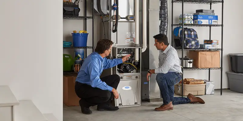 Tech in blue shirt shows male homeowner the work performed inside his home furnace.