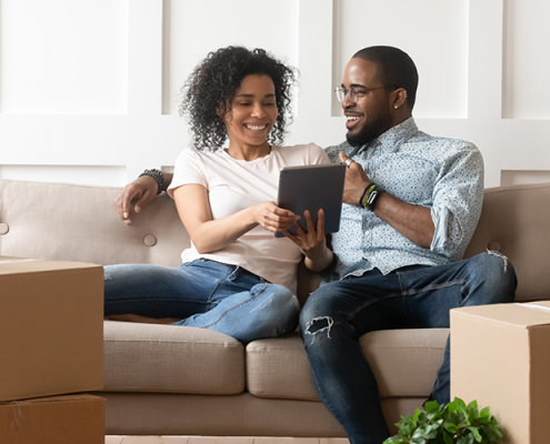 Happy homeowning couple sit on couch and discover HVAC troubleshooting tips.