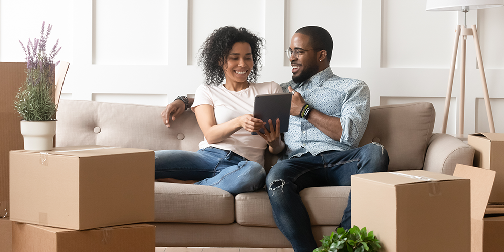 Happy homeowning couple sit on couch and discover HVAC troubleshooting tips.