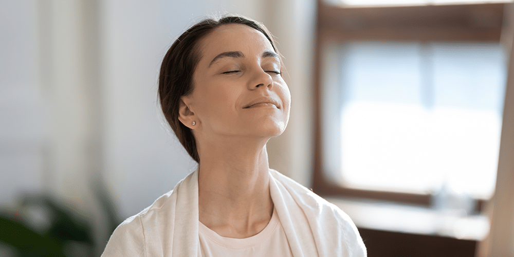 Young female homeowner breathes deeply and reaps great air purifier benefits.