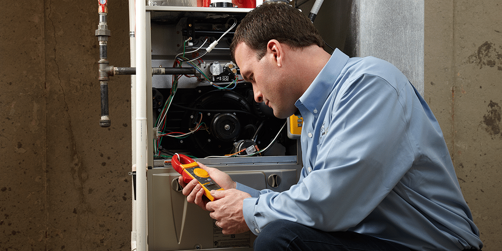 Tech in blue shirt performs annual furnace maintenance in customer's home.