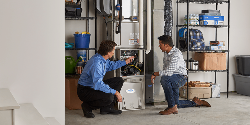 Tech in blue shirt shows male homeowner the work performed inside his home furnace.
