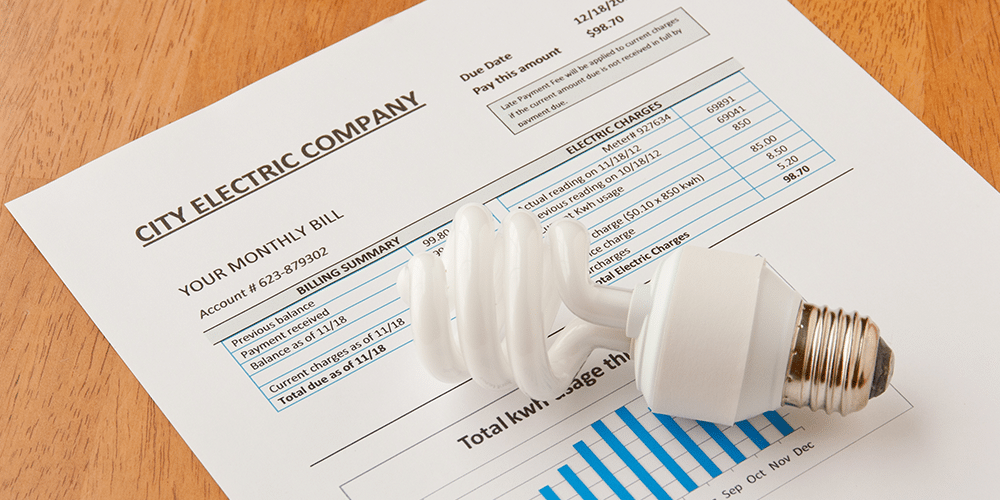Utility bill laid out with lightbulb on table shows need to lower your energy bill.