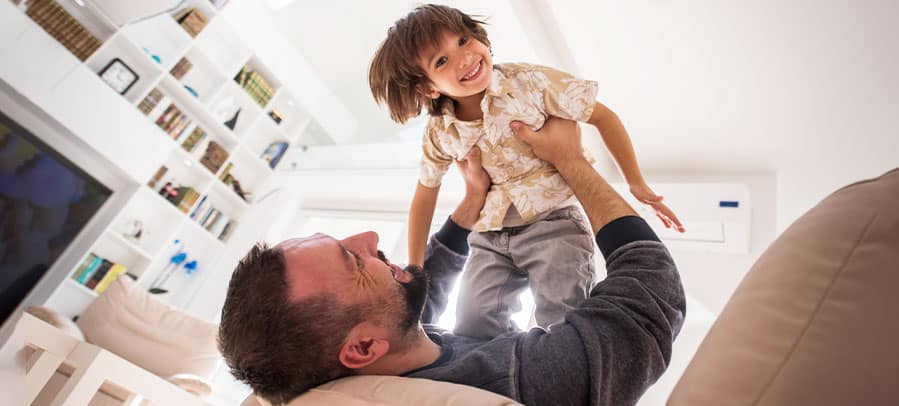 Thermostats Father plays with son on their living room couch.