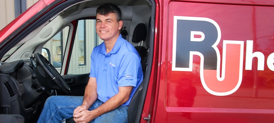 RJ owner Julius sits inside a red RJ Heating truck with the door open, smiling.