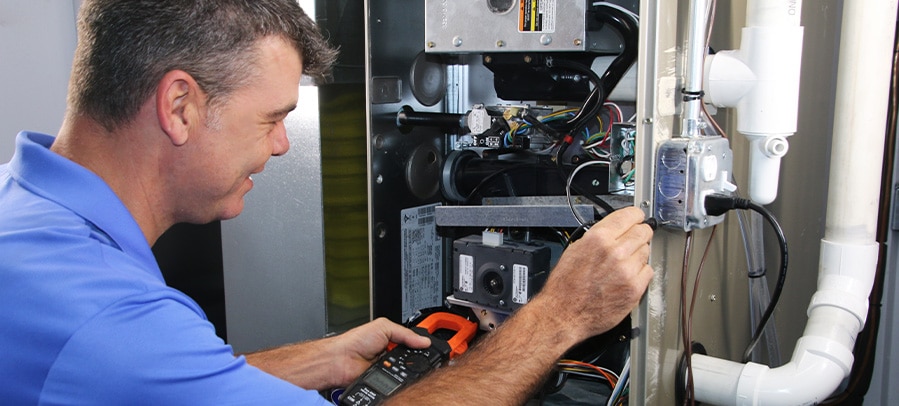 Furnace Maintenance RJ owner Julius smiles as he uses tool to perform furnace maintenance on residential furnace.