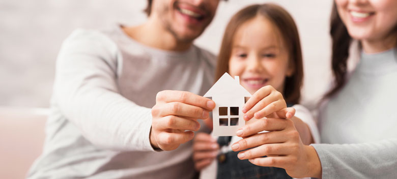 Comfort First FAQs Family of three holding up a paper cutout house.