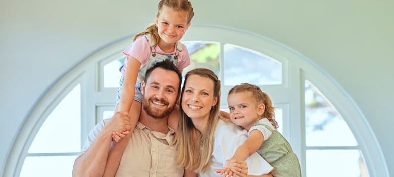 Heat Pump Young family with two kids standing in house smiling at camera.